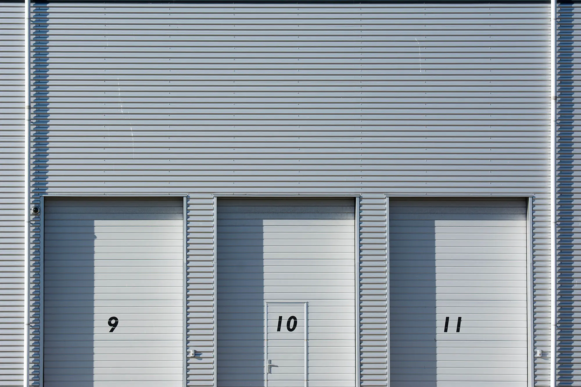 Three closed loading bay doors, numbered 9, 10 and 11, on a grey industrial unit